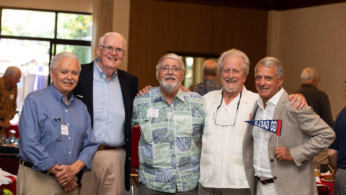 Five alumni smile at the camera, one holding a Go Gaels pennant